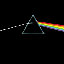 A small grey equilateral and hollow triangle sits slightly above the centre of an opaque black image. A perfectly straight light-grey line enters from the middle of the left edge of the image, and is angled slightly upward to meet the left side of the triangle. Inside the triangle the grey line expands slightly, fading to black as it reaches the centre. On the right side of the triangle a thick bar composed of red, orange, yellow, green, blue, and violet angles downward to the middle right edge of the image.